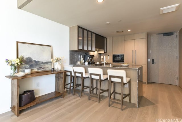 kitchen with decorative backsplash, a peninsula, light wood-style flooring, and a breakfast bar