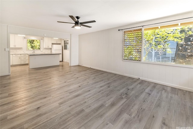 unfurnished living room with a wealth of natural light, light wood-type flooring, baseboards, and ceiling fan