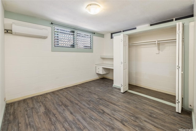 unfurnished bedroom with an AC wall unit, baseboards, a closet, and dark wood finished floors