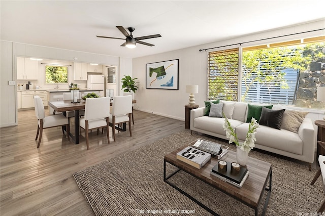 living room featuring plenty of natural light, light wood finished floors, baseboards, and ceiling fan