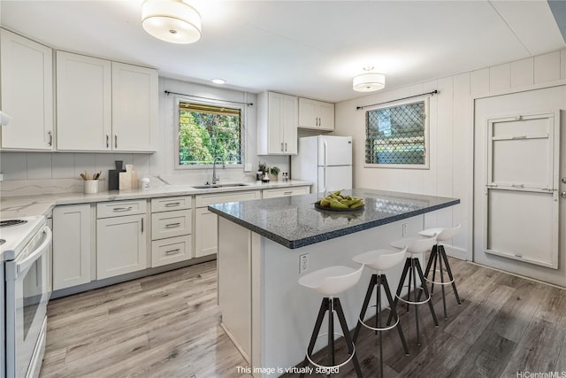 kitchen with white appliances, a kitchen bar, light wood-type flooring, white cabinets, and a sink