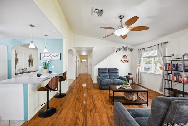 living room with a ceiling fan, visible vents, lofted ceiling, arched walkways, and wood finished floors