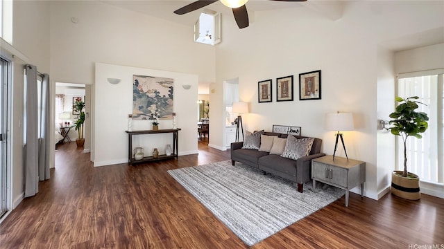 living room with a towering ceiling, dark wood-style flooring, baseboards, and ceiling fan