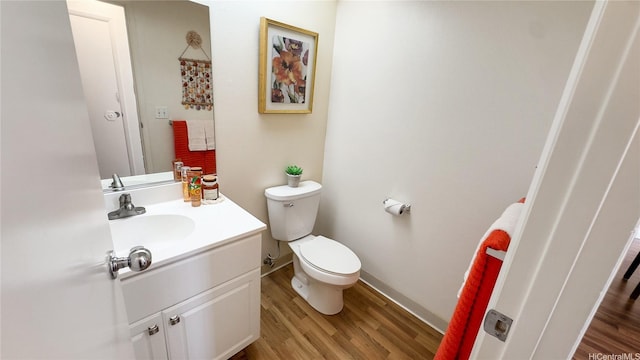 half bathroom featuring vanity, baseboards, toilet, and wood finished floors