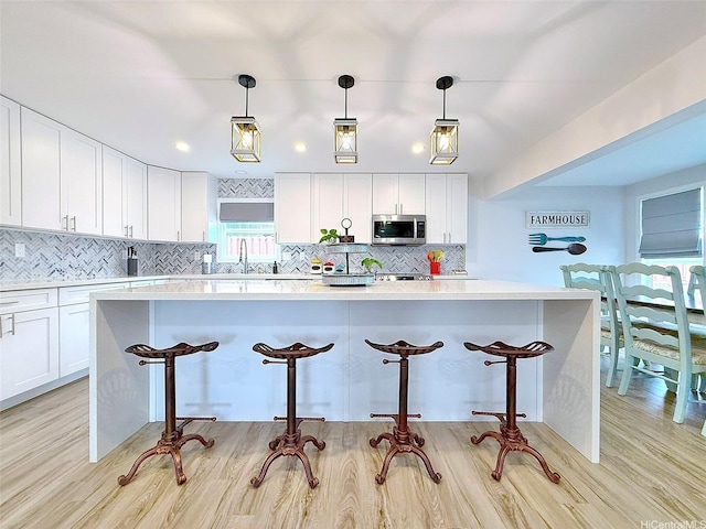 kitchen featuring decorative backsplash, stainless steel microwave, a breakfast bar area, and white cabinets