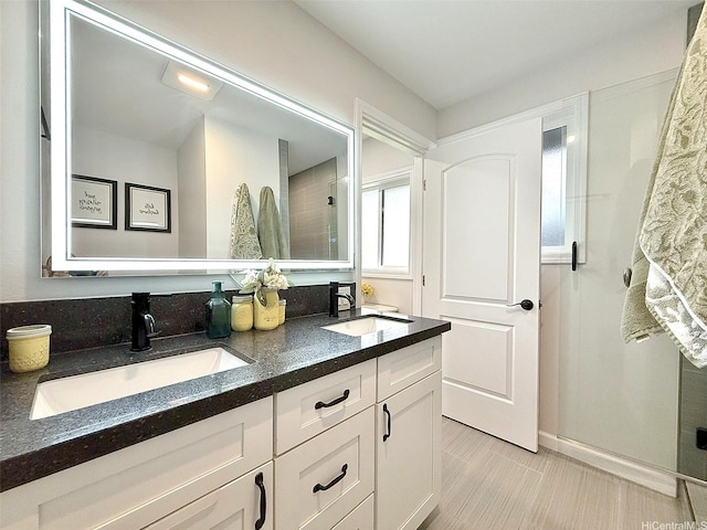 full bathroom featuring a sink, baseboards, walk in shower, and double vanity