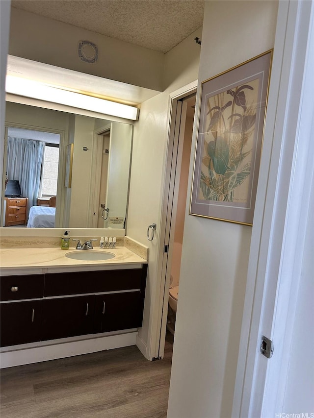 ensuite bathroom featuring ensuite bathroom, toilet, a textured ceiling, vanity, and wood finished floors