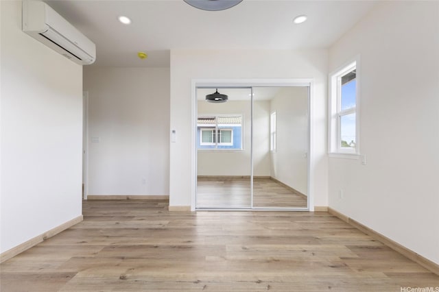 unfurnished bedroom featuring recessed lighting, a wall mounted air conditioner, light wood-type flooring, a closet, and baseboards