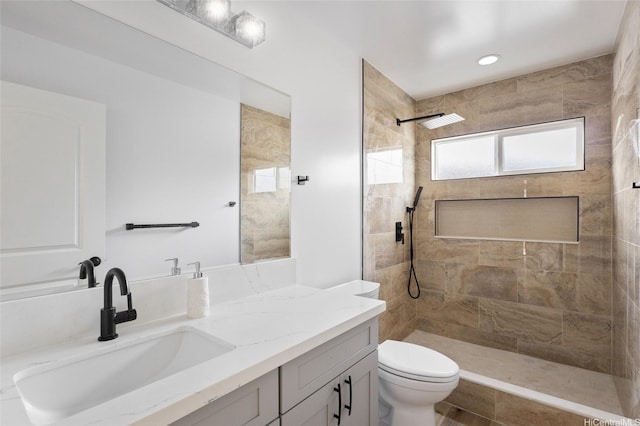 bathroom with a tile shower, toilet, and vanity