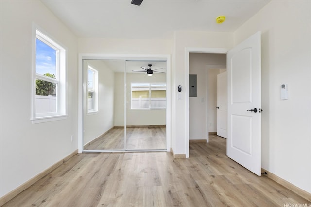 unfurnished bedroom with a closet, light wood-style floors, electric panel, and baseboards