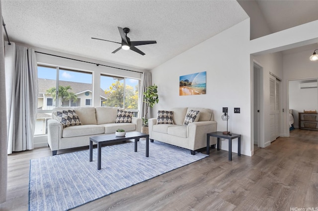 living room with lofted ceiling, a textured ceiling, a wall unit AC, ceiling fan, and wood finished floors
