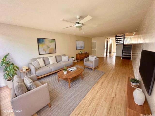 living area featuring stairway, light wood-style flooring, and a ceiling fan