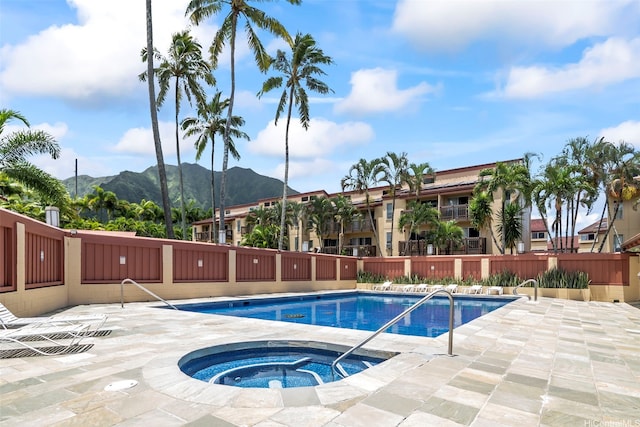 community pool with a hot tub, a patio, fence, and a mountain view
