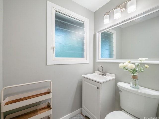 half bathroom featuring toilet, vanity, and baseboards