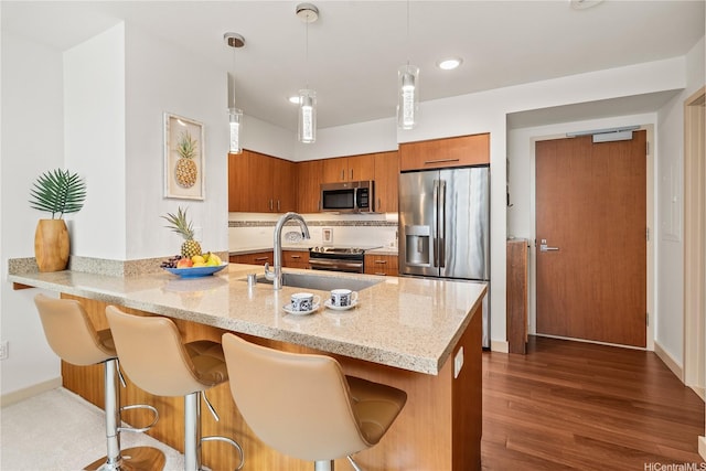 kitchen with brown cabinetry, a peninsula, a breakfast bar, appliances with stainless steel finishes, and a sink
