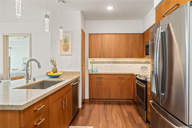kitchen with a sink, brown cabinetry, appliances with stainless steel finishes, and wood finished floors