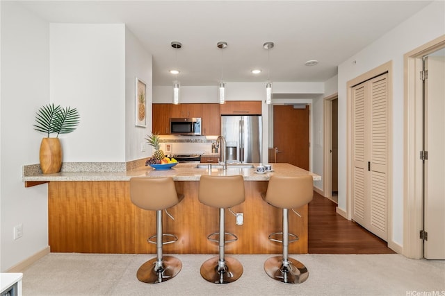 kitchen with pendant lighting, tasteful backsplash, a peninsula, appliances with stainless steel finishes, and brown cabinets