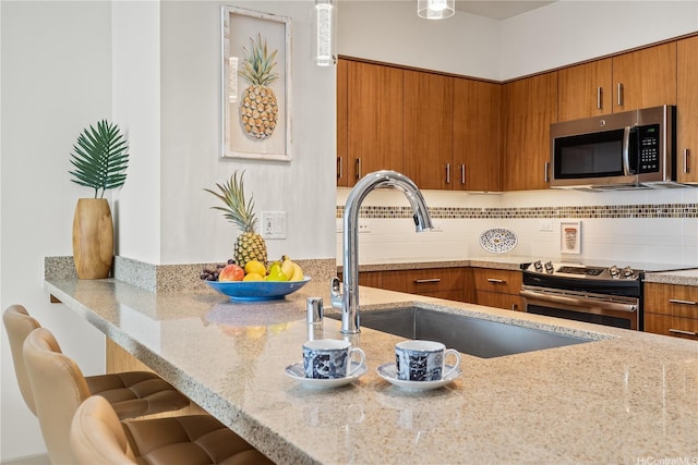 kitchen featuring light stone counters, a sink, stainless steel appliances, brown cabinets, and a breakfast bar area