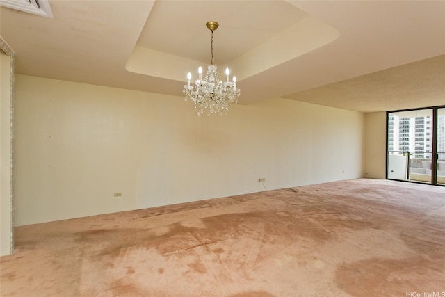 empty room featuring a chandelier, a raised ceiling, visible vents, a wall of windows, and carpet