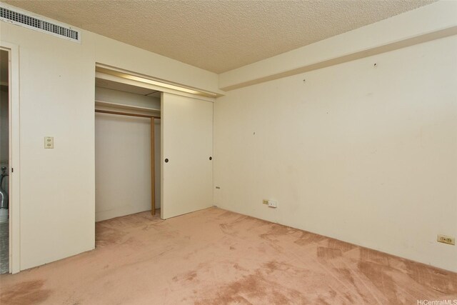 unfurnished bedroom featuring a textured ceiling, a closet, visible vents, and carpet floors