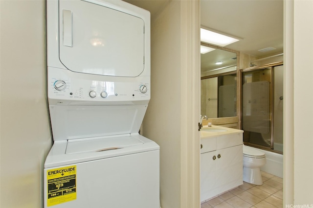 clothes washing area with a sink, light tile patterned floors, stacked washer / dryer, and laundry area