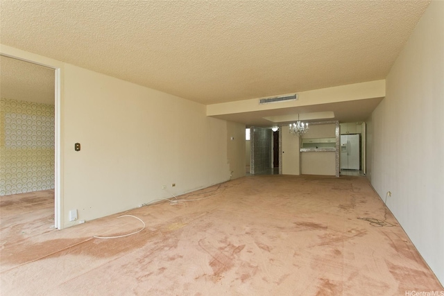 unfurnished living room featuring visible vents, a notable chandelier, carpet, a textured ceiling, and wallpapered walls