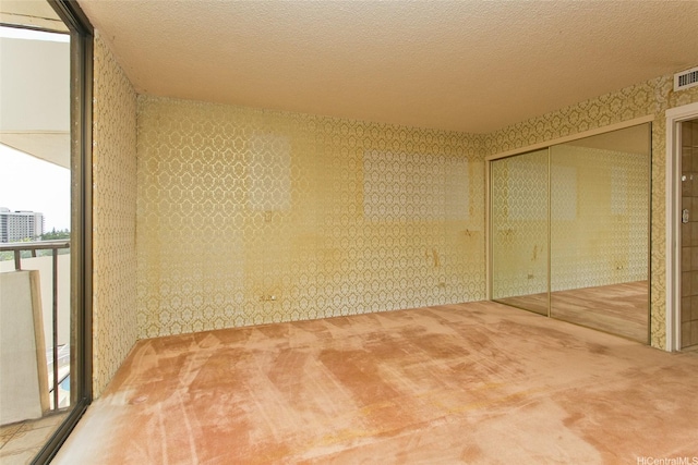 carpeted empty room with a textured ceiling and wallpapered walls