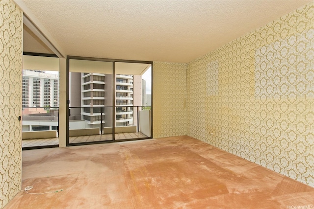 carpeted empty room with wallpapered walls, a wall of windows, and plenty of natural light