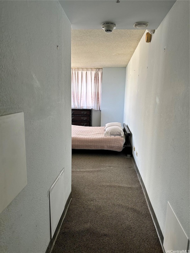 hall with a textured wall, visible vents, baseboards, and carpet floors