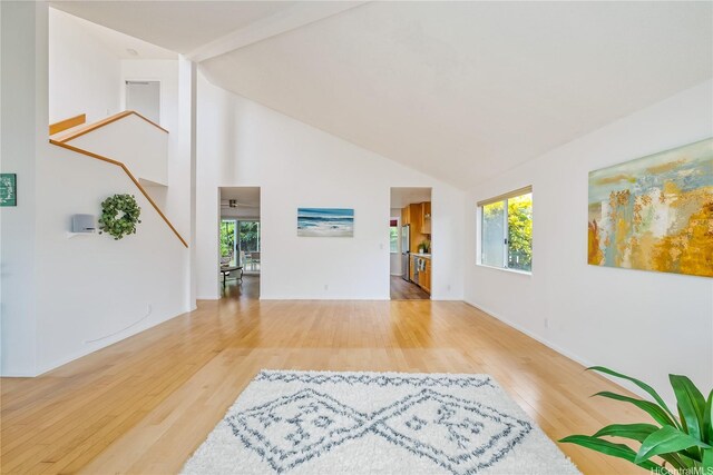 unfurnished living room featuring baseboards, stairs, wood finished floors, and high vaulted ceiling