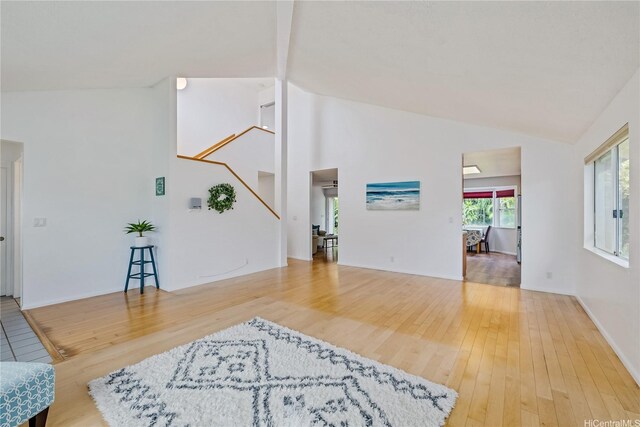 living area featuring high vaulted ceiling, baseboards, stairs, and wood finished floors