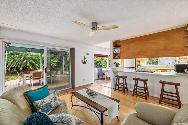 living area with a ceiling fan, a textured ceiling, and light wood-style flooring