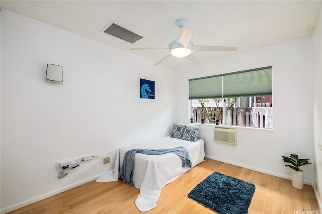 bedroom featuring baseboards, ceiling fan, wood finished floors, and a wall unit AC