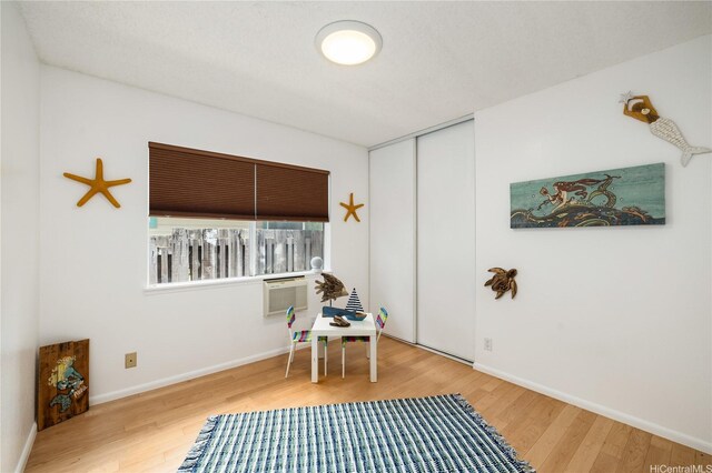 sitting room featuring baseboards, a wall mounted air conditioner, and wood finished floors