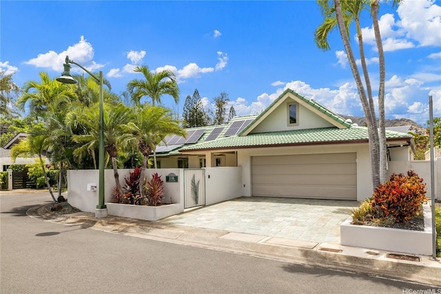 view of front of property featuring a tiled roof, solar panels, fence private yard, an attached garage, and stucco siding