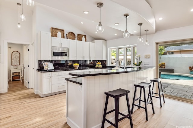 kitchen featuring stainless steel microwave, decorative backsplash, a kitchen breakfast bar, and white cabinetry