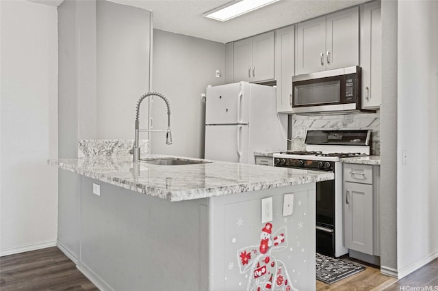 kitchen with a sink, range with gas cooktop, stainless steel microwave, freestanding refrigerator, and gray cabinetry