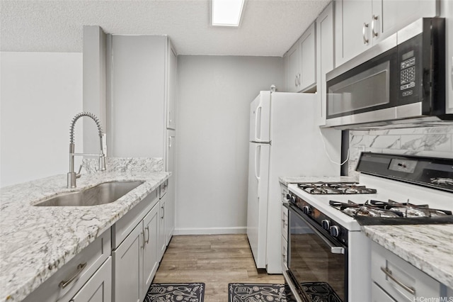 kitchen with white gas range oven, light stone countertops, light wood-type flooring, stainless steel microwave, and a sink