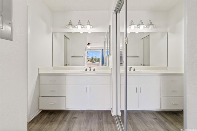 bathroom featuring two vanities, wood finished floors, a ceiling fan, and a sink