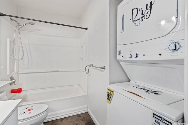bathroom with stacked washer and clothes dryer, bathing tub / shower combination, toilet, stone finish flooring, and baseboards