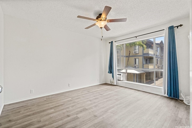 spare room featuring baseboards, a ceiling fan, wood finished floors, and a textured ceiling