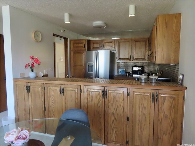 555 Hahaione St Unit 12D, Honolulu, HI 96825 - kitchen with a textured ceiling, brown cabinetry, decorative backsplash, a peninsula, and stainless steel refrigerator with ice dispenser