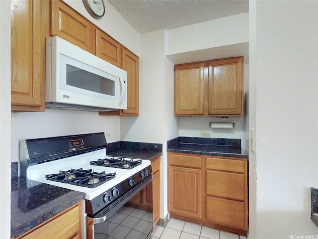 1571 Piikoi St Unit 1601, Honolulu, HI 96822 - kitchen with dark countertops, range with gas stovetop, a textured ceiling, light tile patterned floors, and white microwave