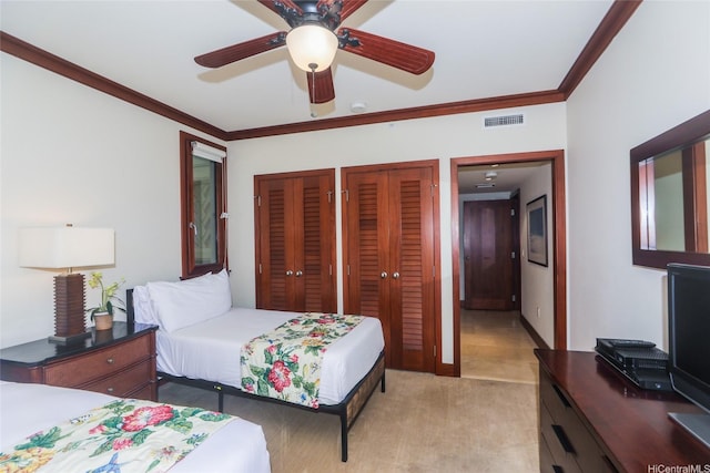 bedroom with light carpet, visible vents, a ceiling fan, two closets, and crown molding