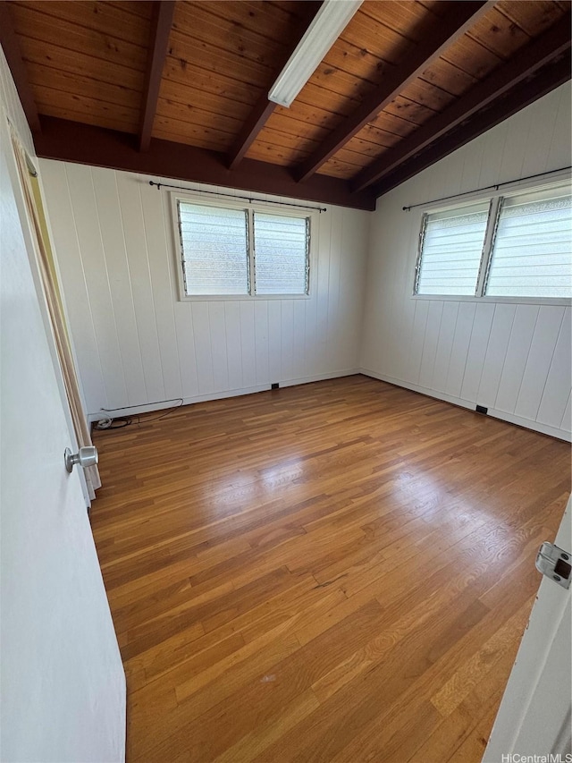 unfurnished room with wooden walls, vaulted ceiling with beams, wood finished floors, and a wealth of natural light