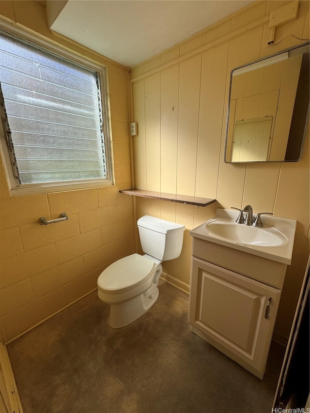 bathroom with toilet, vanity, and concrete block wall