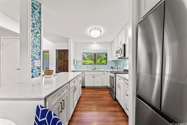 kitchen featuring white cabinets, light stone counters, a sink, decorative backsplash, and appliances with stainless steel finishes