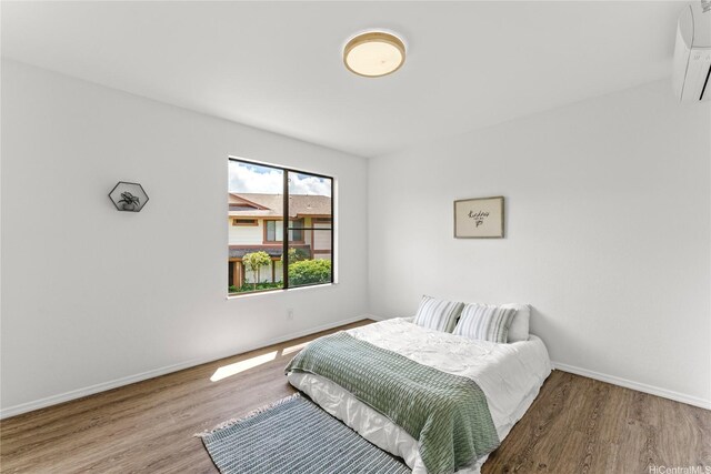 bedroom with wood finished floors, baseboards, and a wall mounted air conditioner