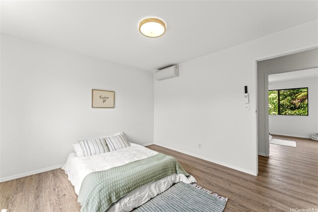 bedroom featuring baseboards, wood finished floors, and a wall unit AC