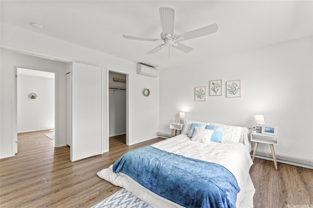 bedroom with wood finished floors, an AC wall unit, a ceiling fan, a closet, and baseboards